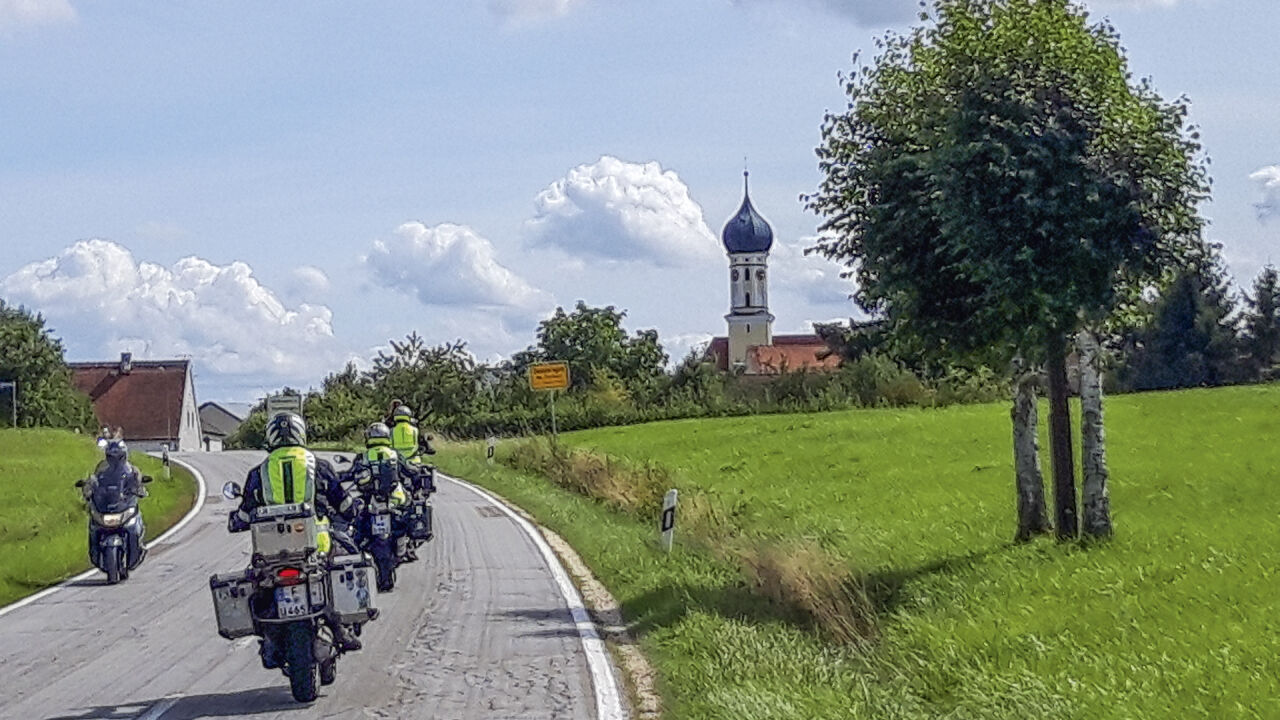 Motorradgruppe auf einer Landstraße, am Rand eine Kirche mit Zwiebelturm